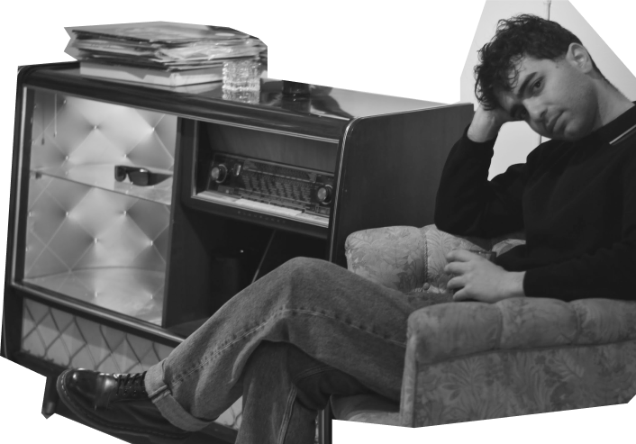 Nikos sitting in a vintage armchair beside an old radio cabinet, in a café in Gothenburg.