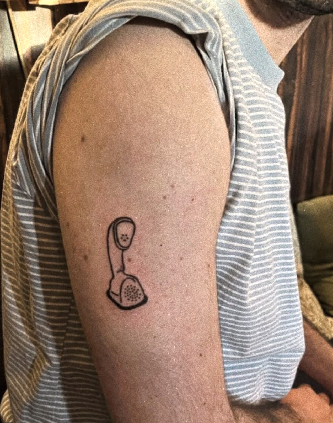 A small line-art tattoo of an Ericofon rotary handset on an upper arm.