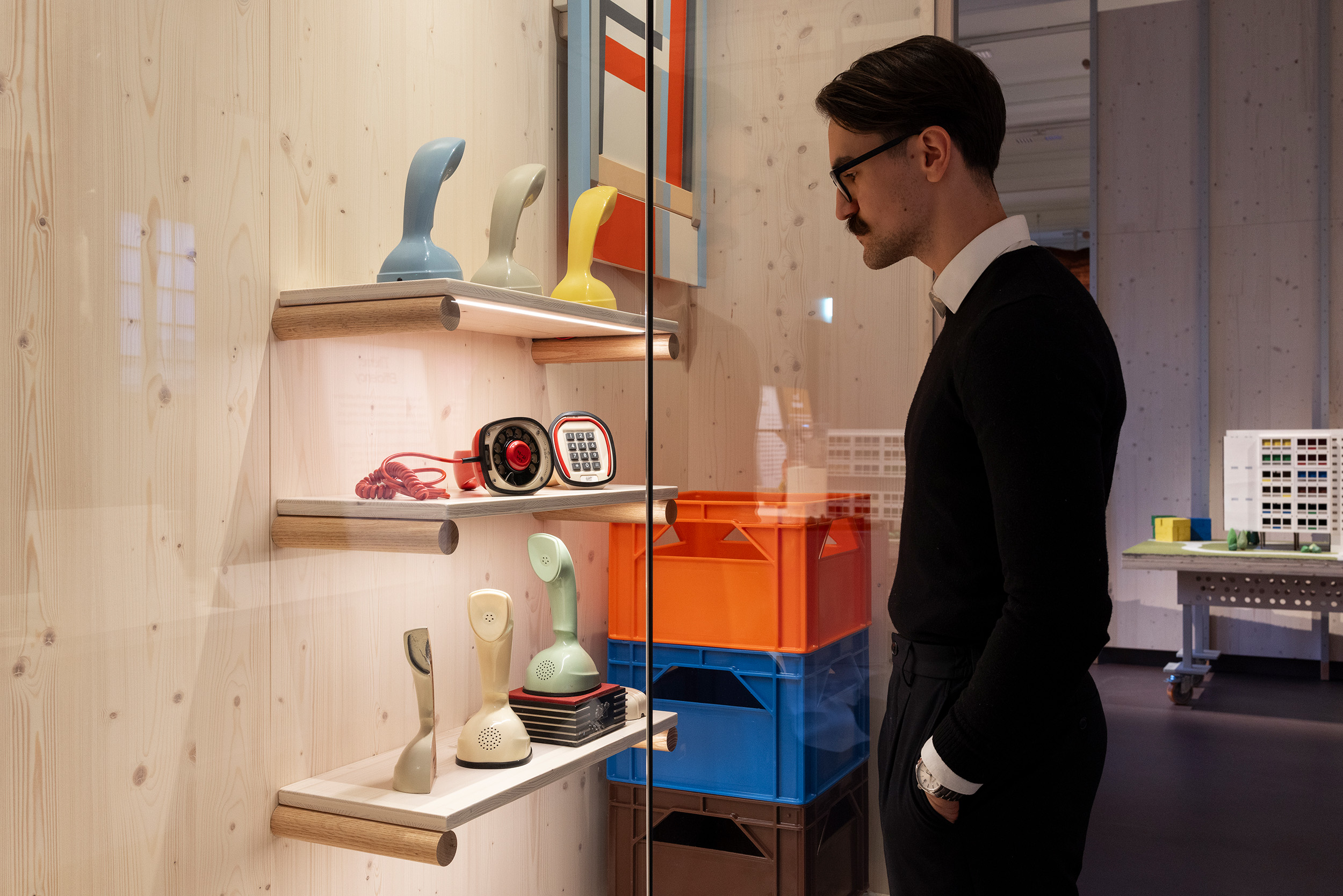 Ericofons in several colours displayed on shelves behind glass at Röhsska, with a visitor looking in.