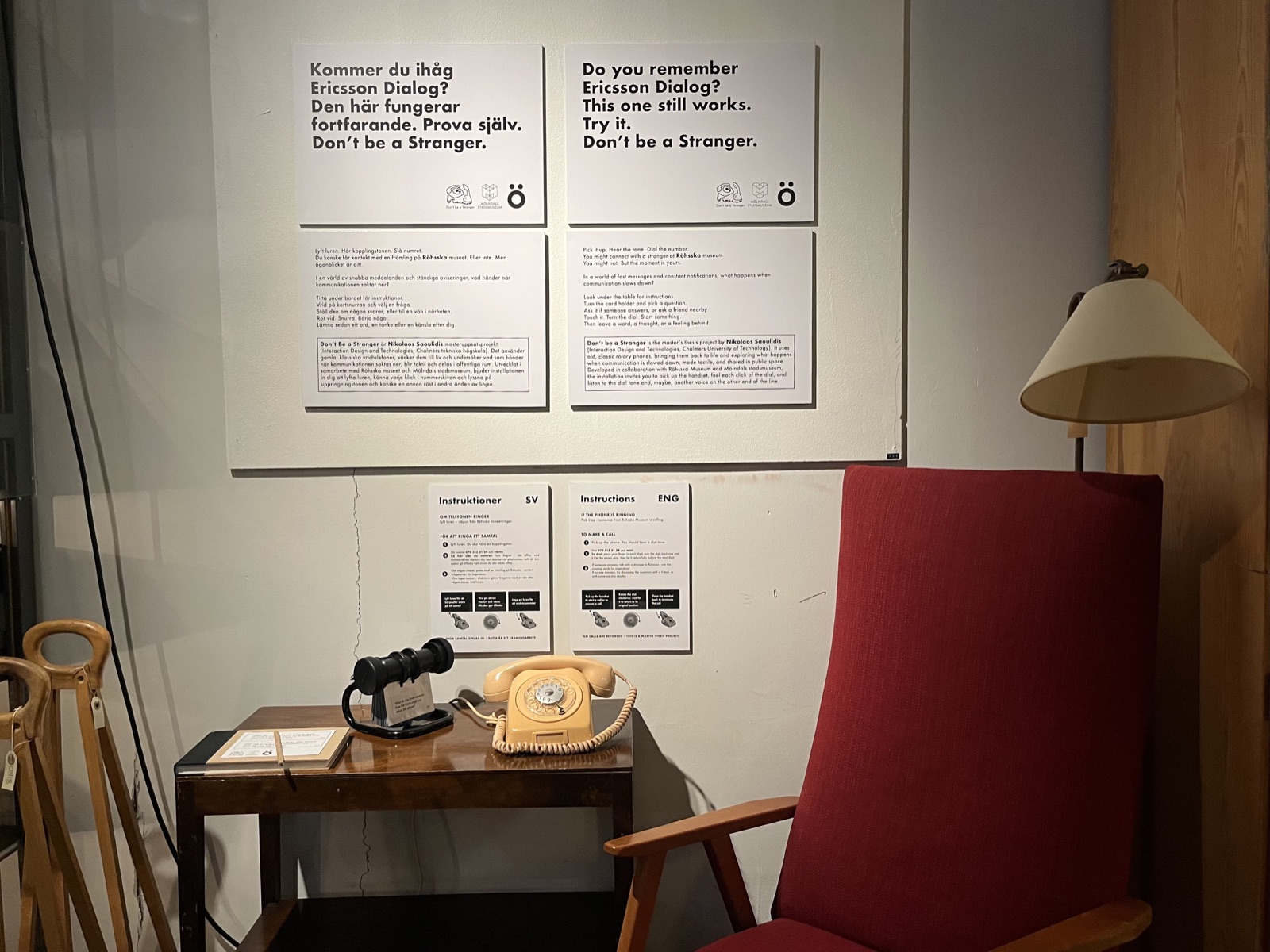 The Mölndal installation in Open Storage: the Ericsson Dialog and a Rolodex on a side table beside a red vintage armchair and a lamp, with bilingual posters on the wall.