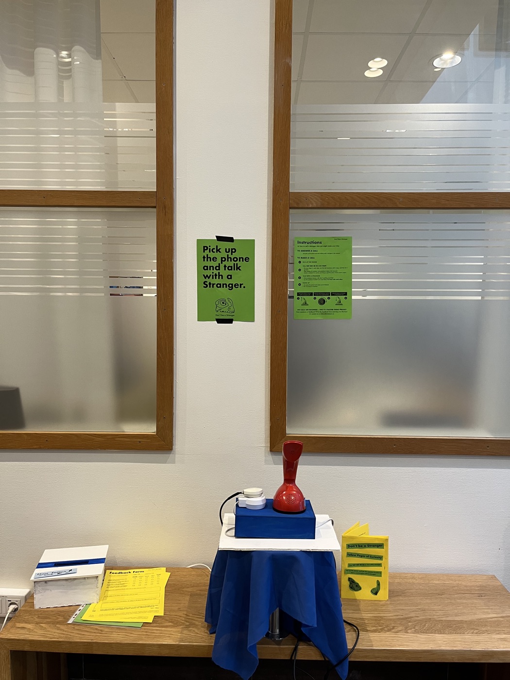 The Ericofon on its blue stand beneath a window, with green posters taped to the glass above it.