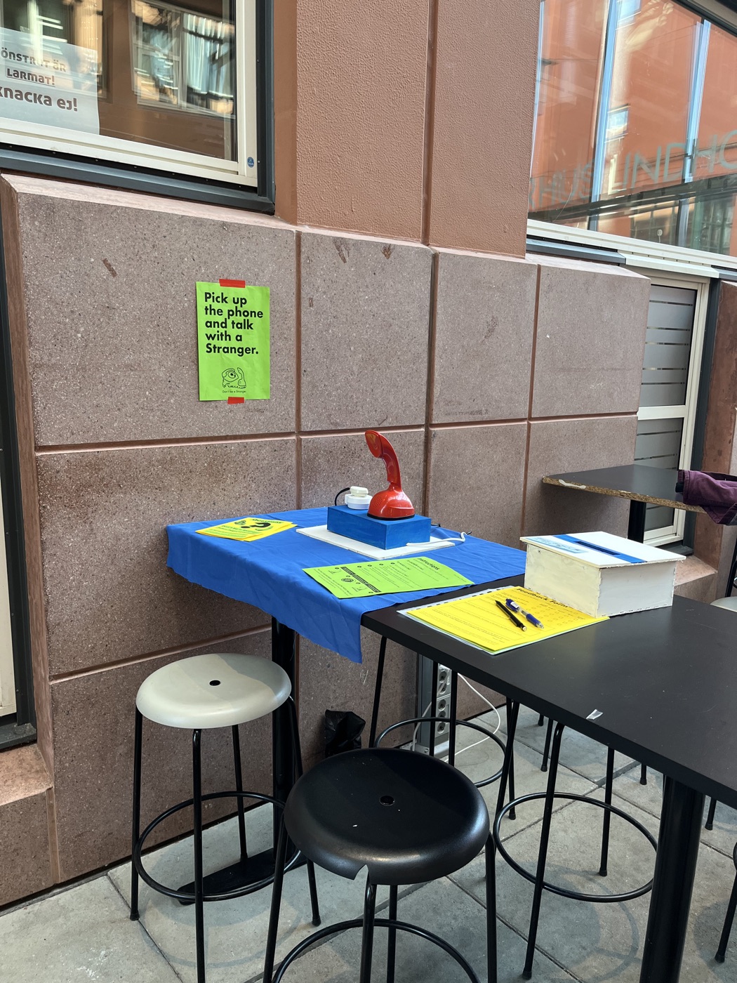 The Ericofon on blue felt on a high table against a padded wall, with a poster and prompt booklets beside it.