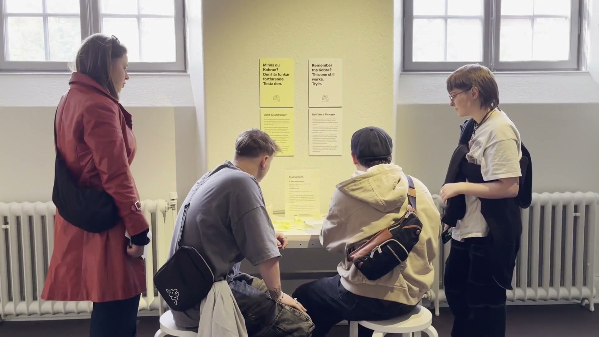 Four visitors gathered around the Don't Be a Stranger table at Röhsska Museum, reading the bilingual posters and instructions.