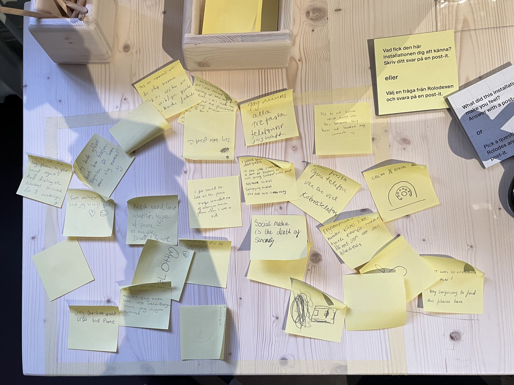 Overhead view of the table at Röhsska covered in yellow post-its, handwritten in Swedish and English, with the pencil box and the prompt card.