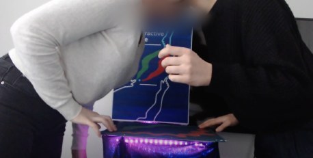 Two students leaning over the table towards each other, the light underneath turning purple.