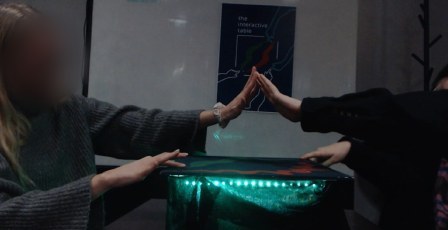 Two students pressing palms together while each touches a point on the table.